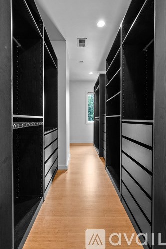 A long hallway with black shelves on the side and wood flooring.