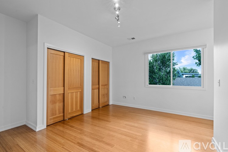 A room with wooden floors and white walls, with a window showing a view of trees and a body of water.