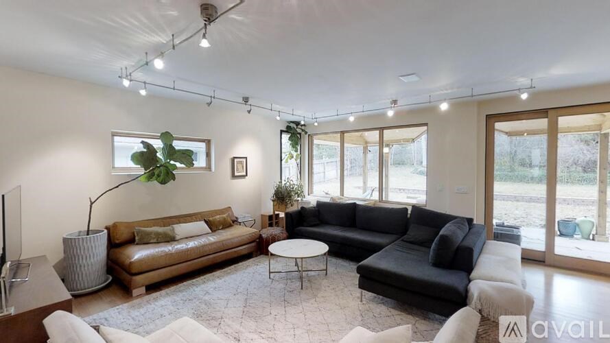A living room with a brown sofa, a black sofa, a white coffee table, and a large window with a view of the outside.