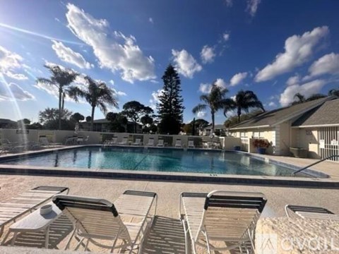 A pool surrounded by chairs and trees under a blue sky.