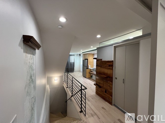 A staircase with a metal railing and wooden steps leads to a room with a wooden cabinet and a white wall.
