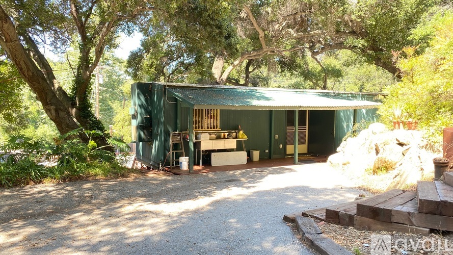 A green building with a porch surrounded by trees.