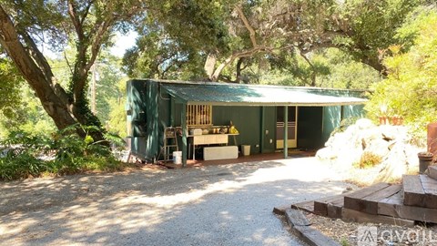 A green building with a porch surrounded by trees.