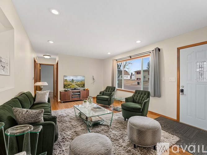 A living room with a green couch, a glass coffee table, and a large window with a view of the outside.