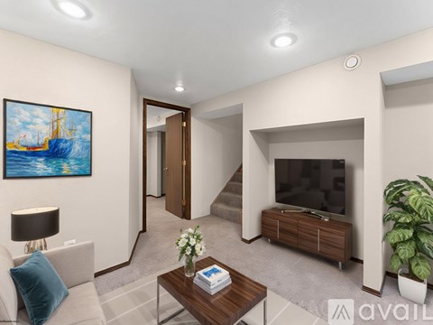 A living room with a grey sofa, a painting on the wall, a wooden coffee table, a grey cushion, a potted plant, a grey carpet, a white wall, a white ceiling, a white door, a