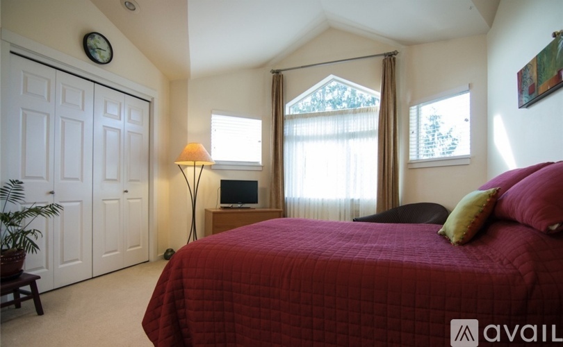A bedroom with a red bedspread and a red pillow on the bed.
