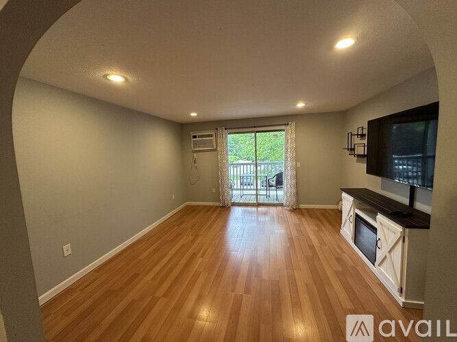 A spacious room with wooden flooring and a sliding glass door leading to a balcony.