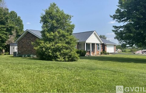 A house with a brick chimney and a white porch is surrounded by a grassy lawn and trees.