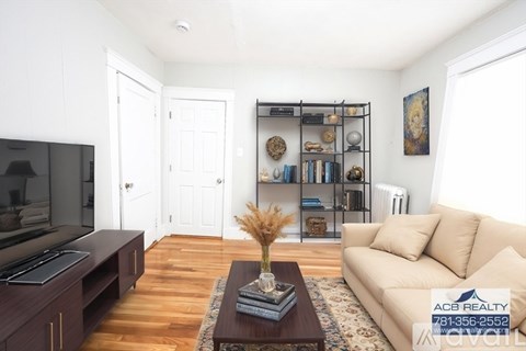 A living room with a white couch, a coffee table, and a bookshelf with various items on it.