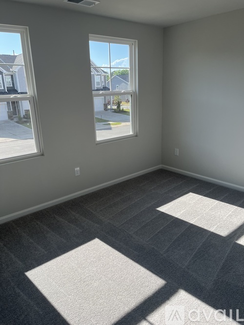 A room with grey carpet and two windows.