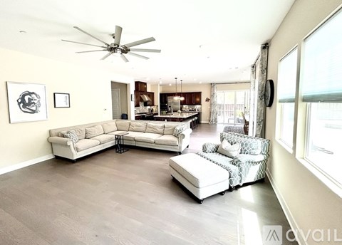 A spacious living room with a white sofa set and a ceiling fan.