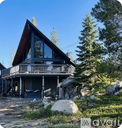 A modern house with a large deck and a balcony is surrounded by trees and rocks.