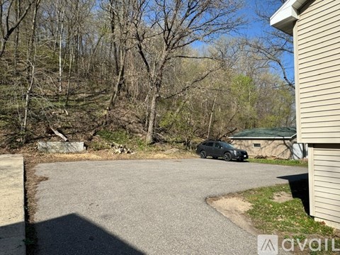 A car is parked in a driveway with trees in the background.