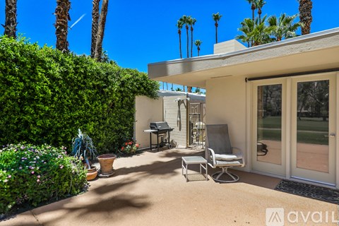 A patio with a table and chairs is surrounded by a green hedge.