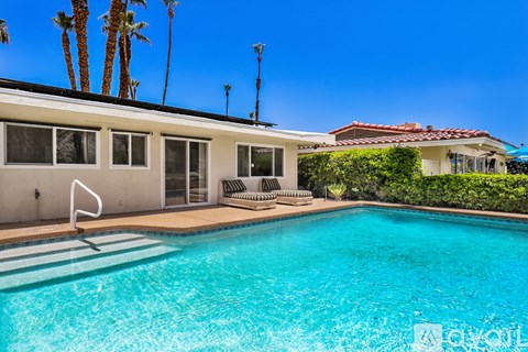A pool in front of a house with a white fence.