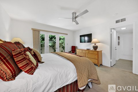 A bedroom with a large bed, a ceiling fan, and a flat-screen TV mounted on the wall.