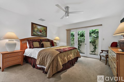 A bedroom with a large bed, a ceiling fan, and a painting on the wall.