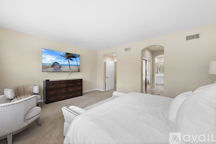 A bedroom with a large bed, a sofa, and a television displaying a beach scene.