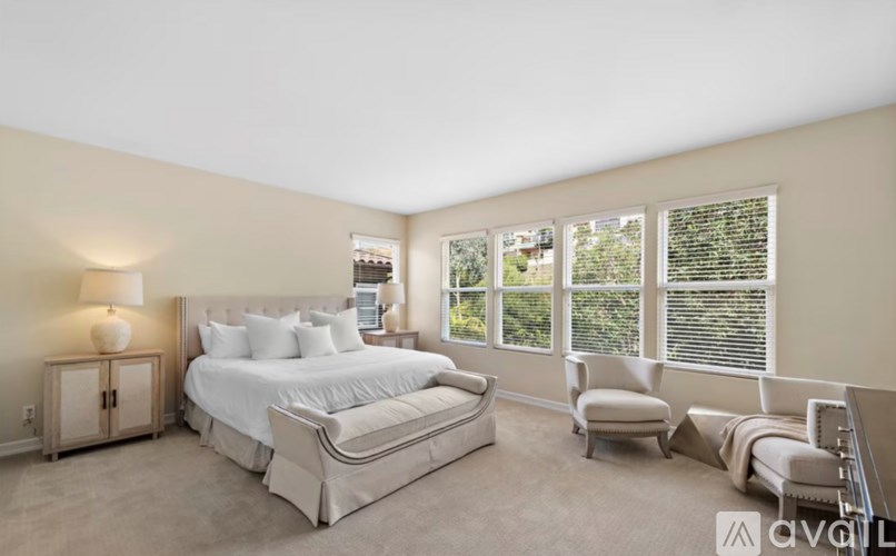 A bedroom with a large bed, a chair, and a window with blinds.