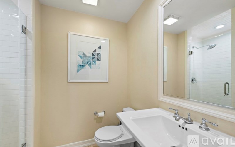 A bathroom with a toilet, sink, mirror, and a picture on the wall.