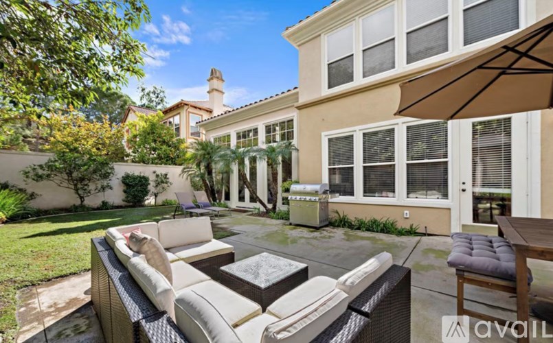 A patio with a table and chairs is surrounded by a house and trees.