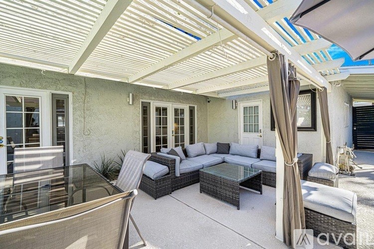 A patio with a glass table and chairs under a white awning.