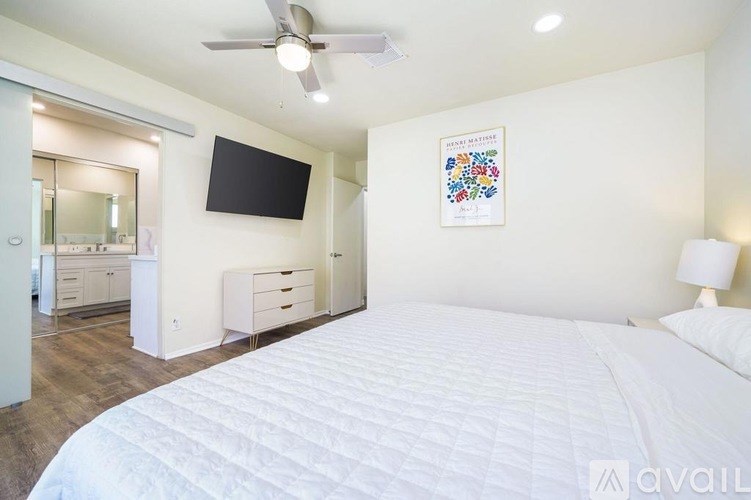 A bedroom with a large bed, a ceiling fan, and a flat-screen TV mounted on the wall.
