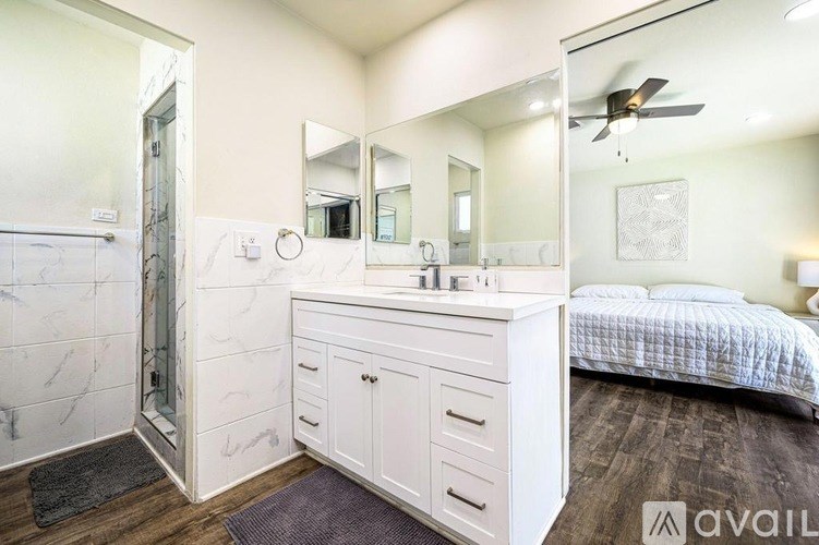 A bedroom with a marble shower and a white vanity with a mirror above it.
