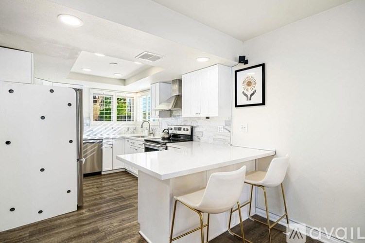 A modern kitchen with white cabinets and a white island with two chairs.