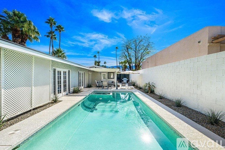 A pool in a backyard with a white fence and a patio area.