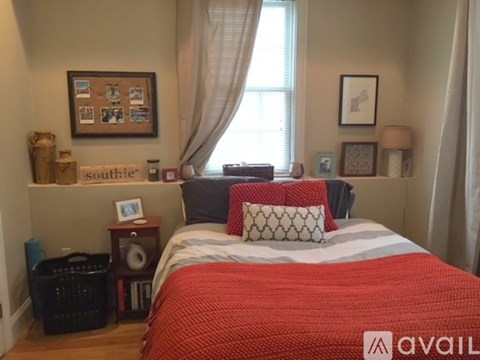 A bedroom with a red bedspread and a window with curtains.