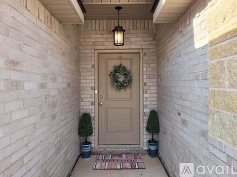 A door with a wreath on it is flanked by two small trees.