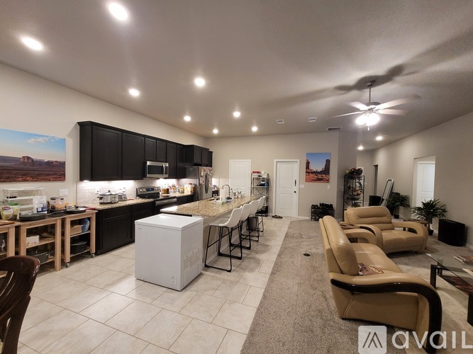 A spacious kitchen and living room with a refrigerator, chairs, and a ceiling fan.
