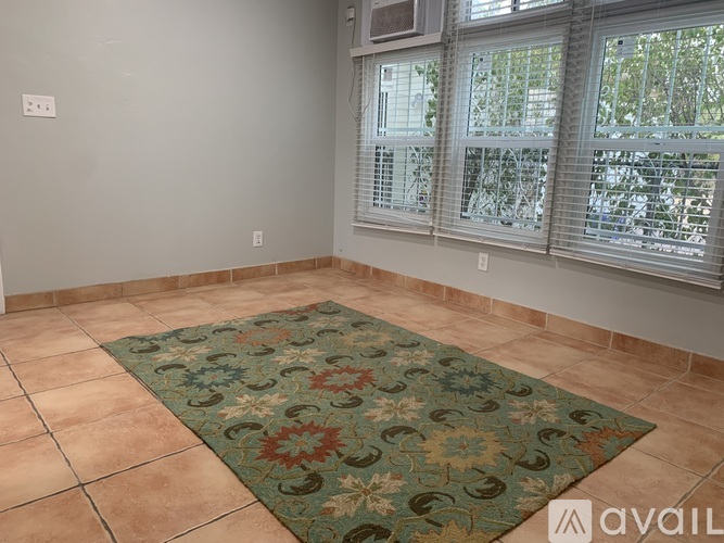 A room with a rug on the floor and a window with blinds.