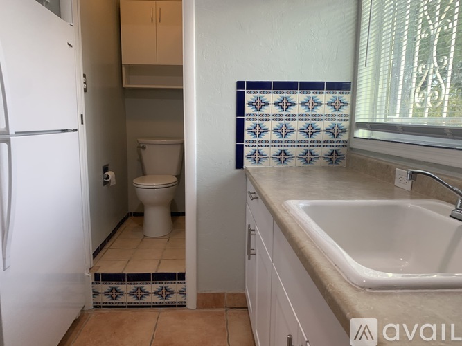 A kitchen with a white fridge, a white toilet, and a white sink.