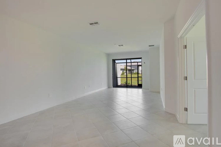 A spacious room with white walls and a tiled floor leading to a balcony.