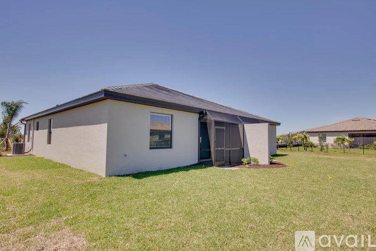 A house with a grey roof and a white wall is surrounded by a green lawn.