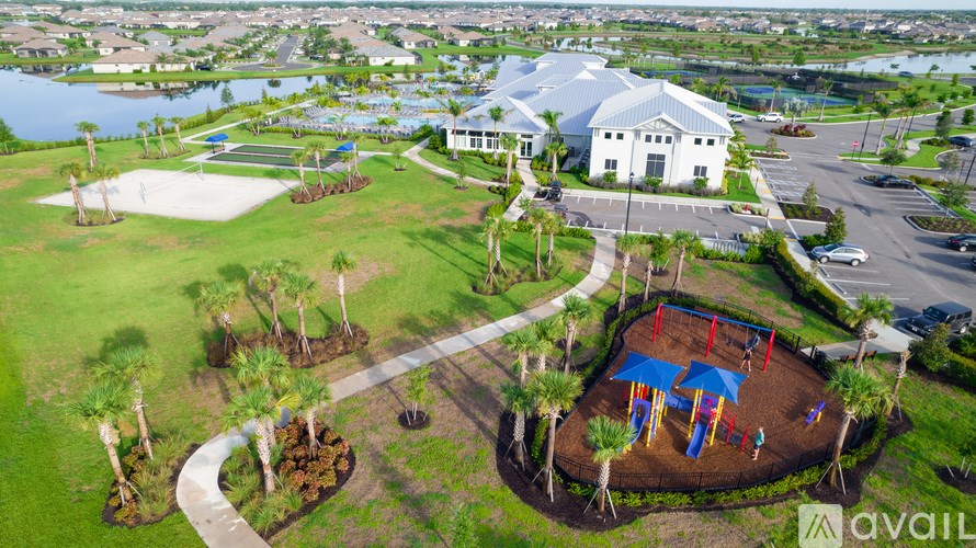 A playground with a slide and a red swing set is surrounded by a grassy area and a white building with a blue roof is in the background.