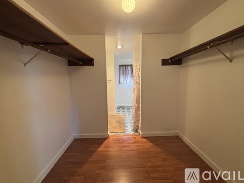 A hallway with wooden floors and white walls leading to a door with a curtain.