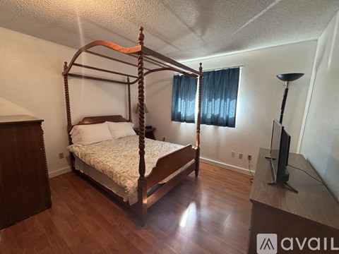 A bed with a wooden frame and canopy in a room with a TV and a window with curtains.