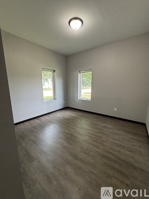 A room with wooden flooring and two windows.