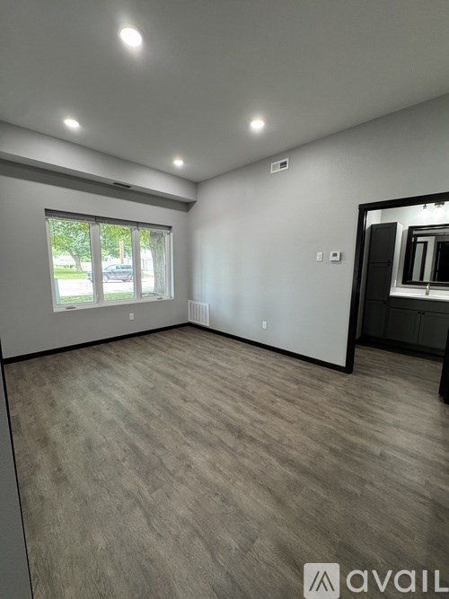 A spacious room with a large window and wooden flooring.