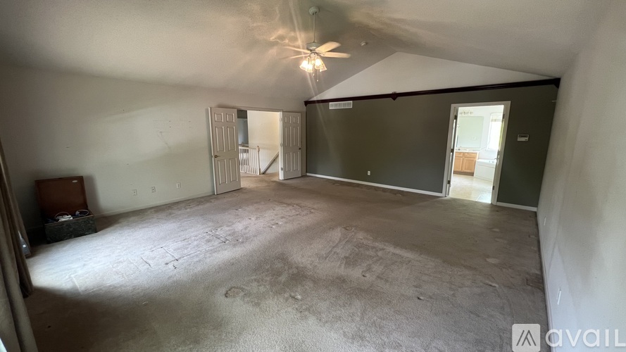 A spacious room with a ceiling fan and a door leading to another room.