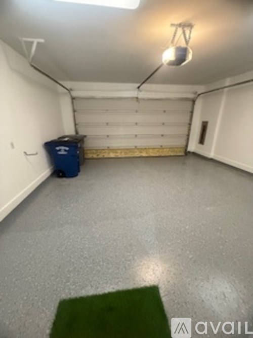 A blue trash can sits in a white garage.