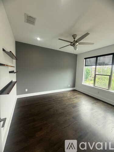 A room with a ceiling fan and a window overlooking greenery.