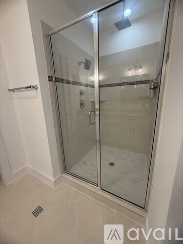 A glass shower stall with a white wall and a drain in the floor.