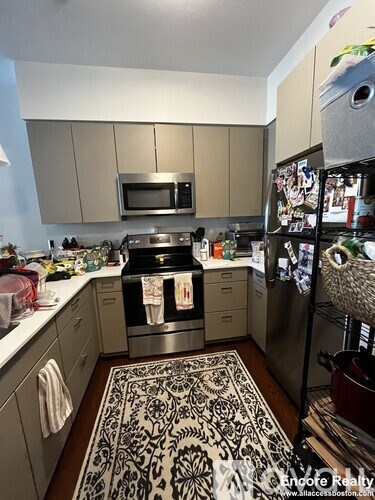 A kitchen with a refrigerator full of magnets and a patterned rug on the floor.
