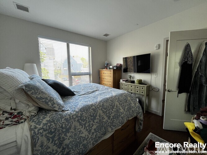 A bedroom with a bed, a dresser, and a window with blinds.
