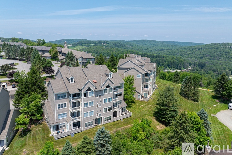 A large, multi-story residential building with a grey exterior is surrounded by greenery and other similar structures in a well-maintained neighborhood.