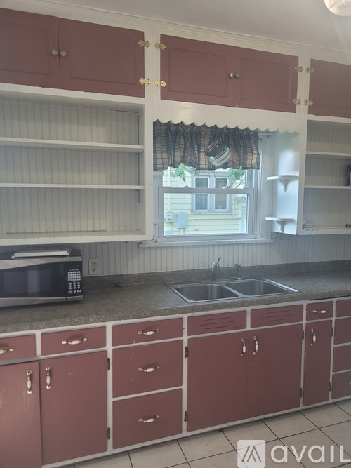 A kitchen with red cabinets and a window with a curtain.